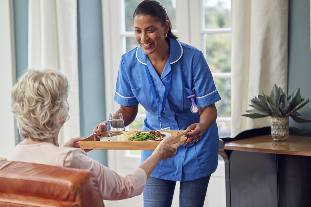 Woman giving supported living services to a senior by serving her client's dinner